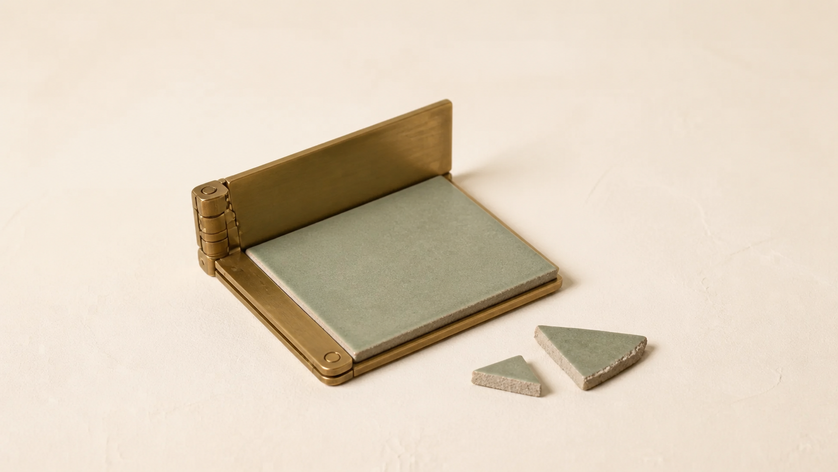 A hinged brass writing tablet with a sage ceramic page, next to loose broken fragments